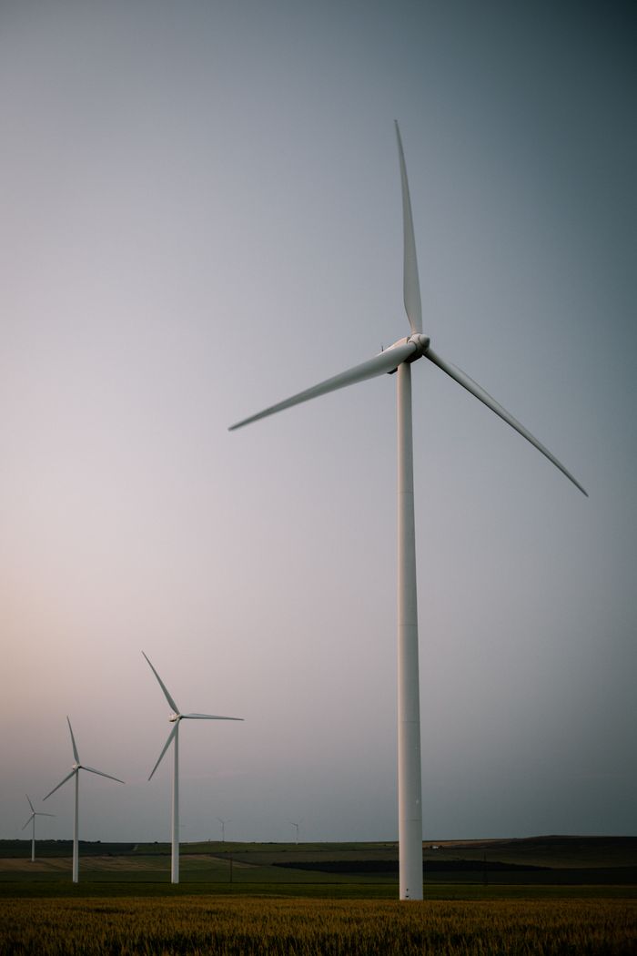 Home Three wind turbines stand tall in an open field, symbolizing renewable energy.