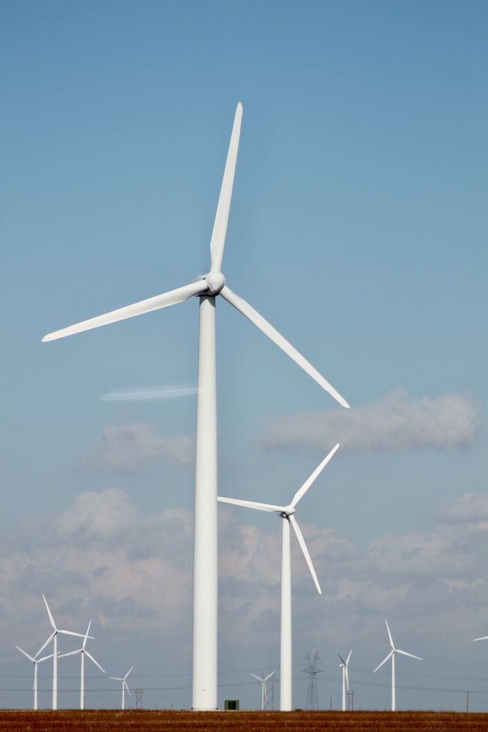 Home A series of tall wind turbines generating renewable energy in a clear open field.