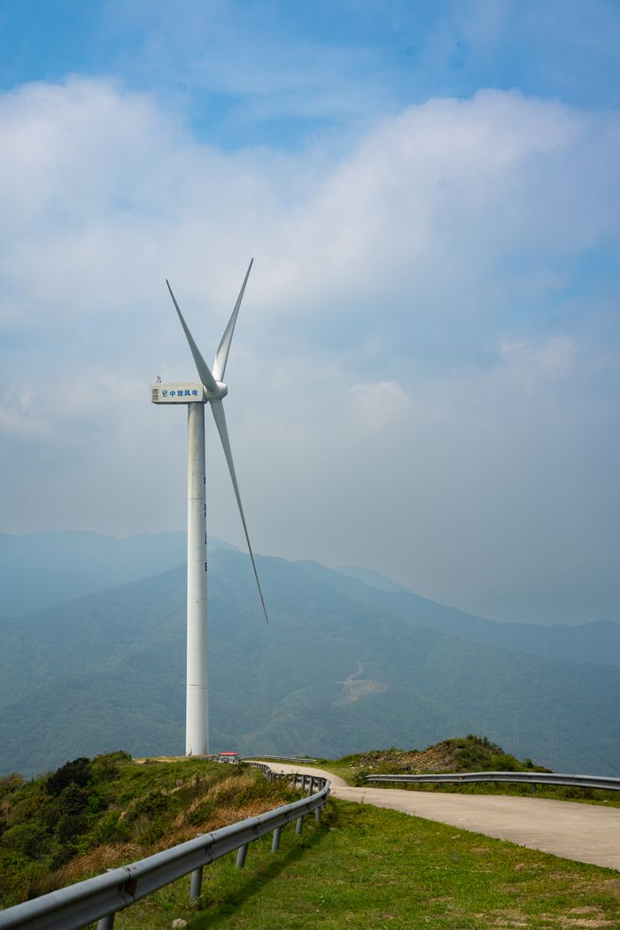 gallery-05 A wind turbine stands tall against a picturesque mountain backdrop, highlighting renewable energy.