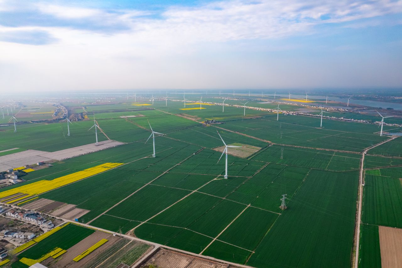 Home Expansive aerial view of wind turbines across farmland in Jiujiang, China, highlighting sustainable energy.
