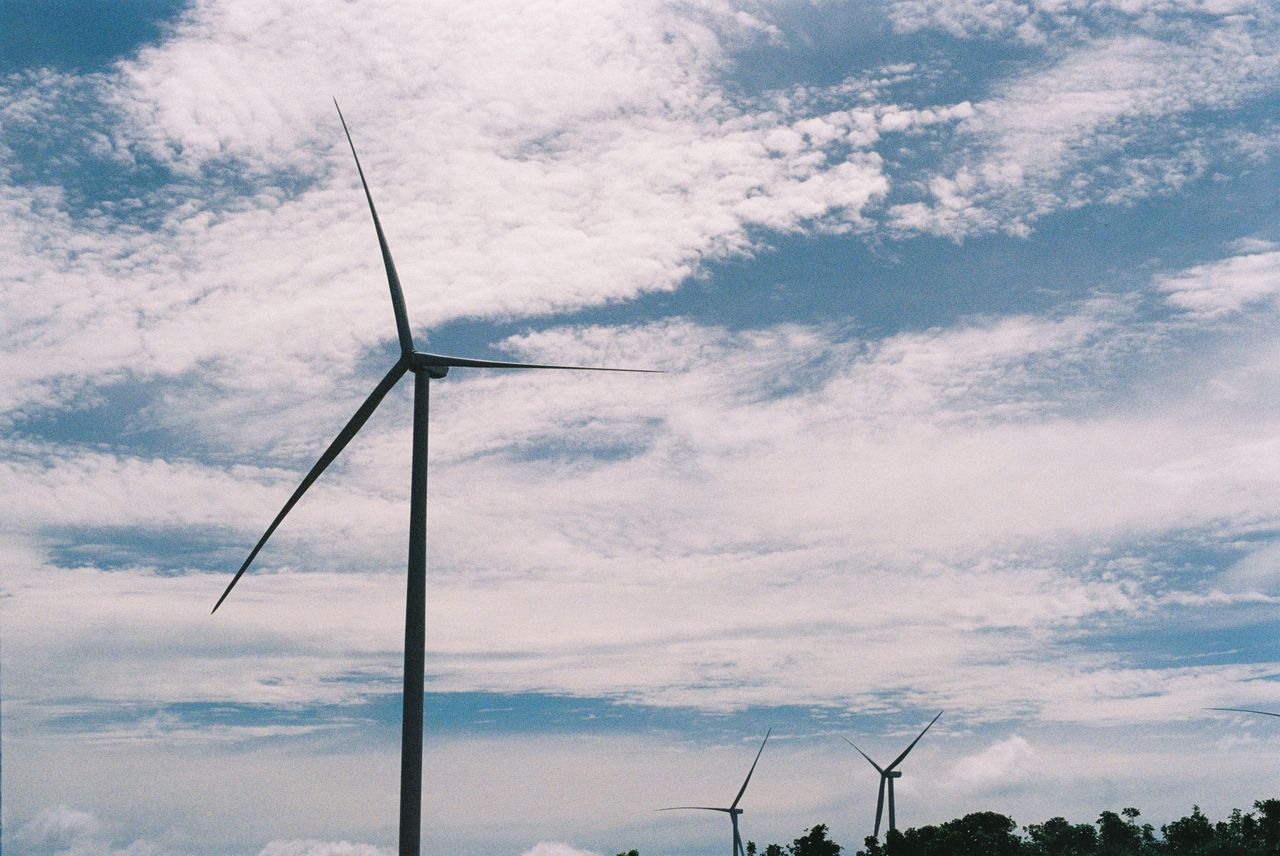 About Scenic view of wind turbines against a cloudy sky, representing renewable energy.