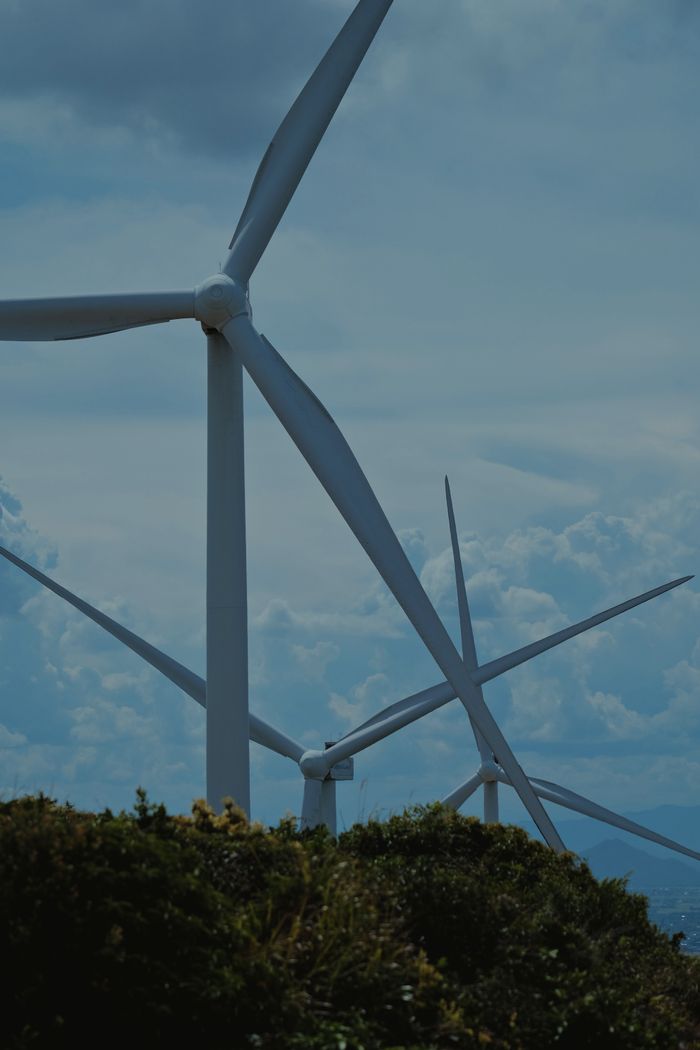 gallery-04 Wind turbines in a lush landscape under blue skies, symbolizing sustainable energy.