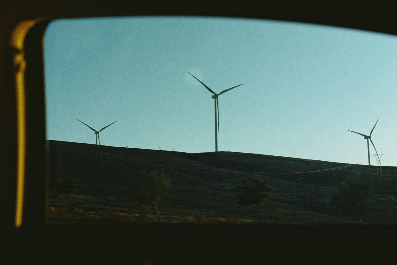 Offerings Wind turbines on a hill silhouetted against a clear sky at sunset, symbolizing renewable energy.